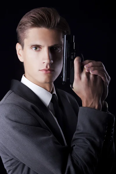 Unga attraktiva macho i kostym med pistol på svart bakgrund — Stockfoto