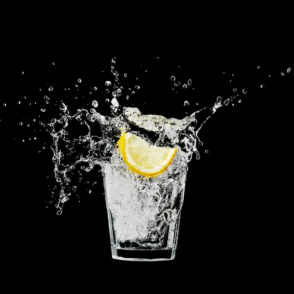 Salpicar en un vaso con limón y hielo sobre un fondo negro —  Fotos de Stock