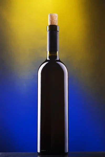 Bottle of red wine against blue and yellow background — Stock Photo, Image