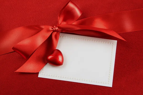 Kırmızı yay ve hediye saten zemin üzerine beyaz kart — Stok fotoğraf