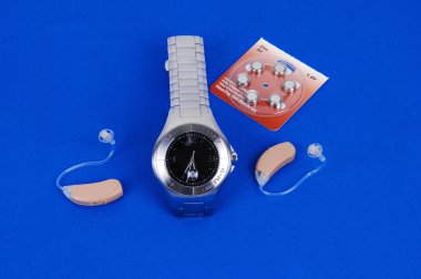 A modern hearing aid and the watch to control the volume of the aid with replaisment batteries on royal blue fabric. clipart