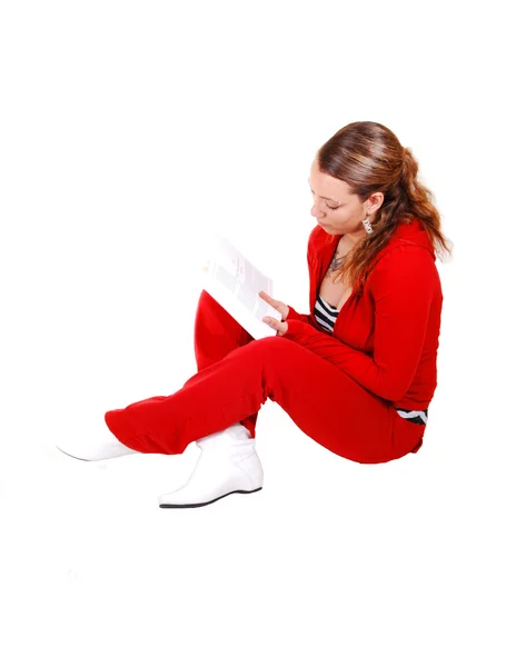 一个年轻漂亮的女子红色运动服和白色皮靴 坐在演播室里 在地板上 读一本书 对于白色背景 — 图库照片