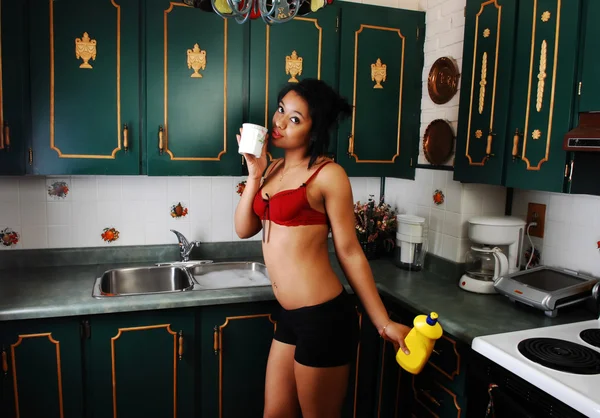 一名年轻的漂亮西班牙裔女子洗碗在厨房与绿色的碗橱 戴着只是一条黑色短裤和红色的胸罩 — 图库照片