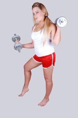 A young girl in a red shorts and white top and silver dumbbells in her hands, try to try to get some exercise to get fit and loose some weight. clipart