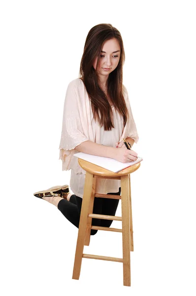 一个风华正茂的少年 跪在弗洛尔 紧身裤和长黑发的头发和一把椅子在她面前 为白色背景上的一个笔记本 — 图库照片