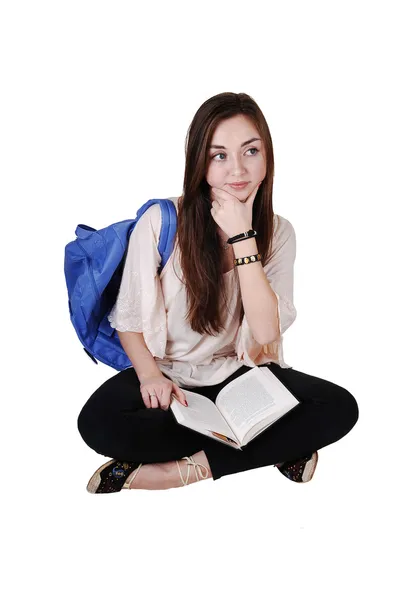 少年坐在地板上有一个蓝色的书包越过她的肩膀在一件衬衫和黑色的紧身裤 拿着一本书在她的大腿上 对于白色背景 — 图库照片