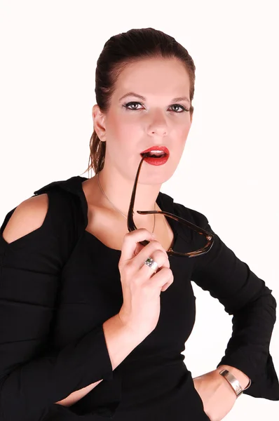 年轻光的红头发的女人在黑色礼服站在白色的背景 工作室在她嘴里有她的太阳镜 — 图库照片