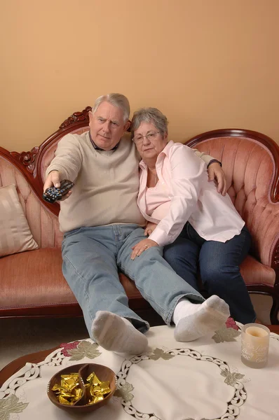 そこのリビング ルームのソファーに座っていると 白い背景のためのテレビでチャンネルを切り替え 年配のカップル — ストック写真
