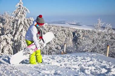 güzel bir kadın snowboard ile dağın zirvesinde duruyor. karla kaplı çam ağaçları ve mavi gökyüzü fonunda.