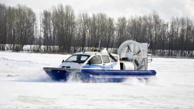 Hovercraft rides on the frozen river, picking up snow dust. Winter clipart