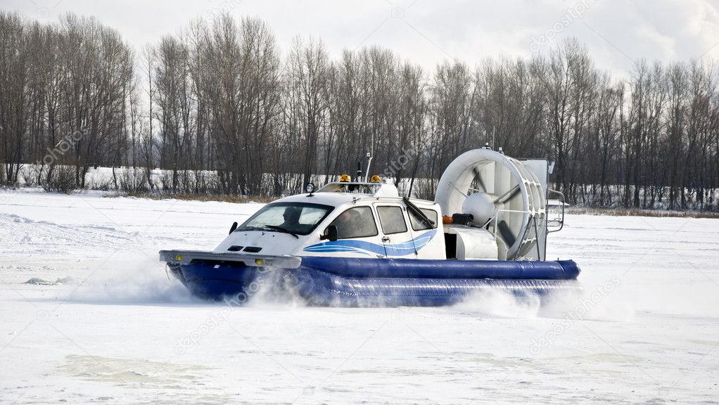 Hovercraft rides on the frozen river, picking up snow dust. Winter