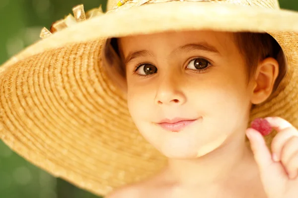 Niño travieso en sombrero de paja muestra frambuesa —  Fotos de Stock