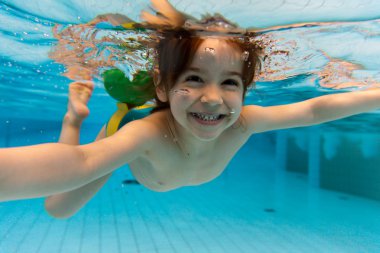 The girl smiles, swimming under water in the pool