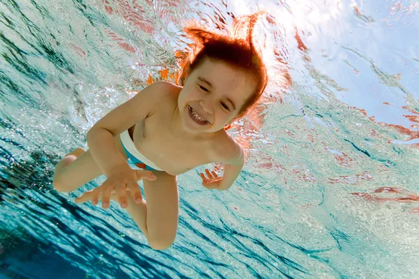 La chica sonríe, nadando bajo el agua en la piscina — Foto de Stock