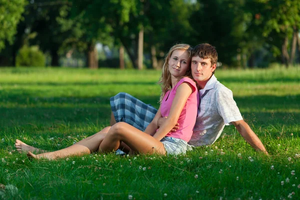 Deux jeunes amoureux assis sur la pelouse dans le parc et regarde dans — Photo