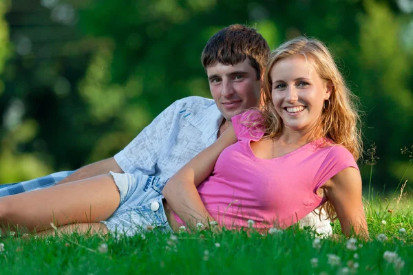 Una pareja relajándose en el parque, tumbada en la hierba, iluminada en el ev —  Fotos de Stock