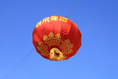 A red Chinese lantern with gold characters and decorations set against a vibrant blue sky clipart