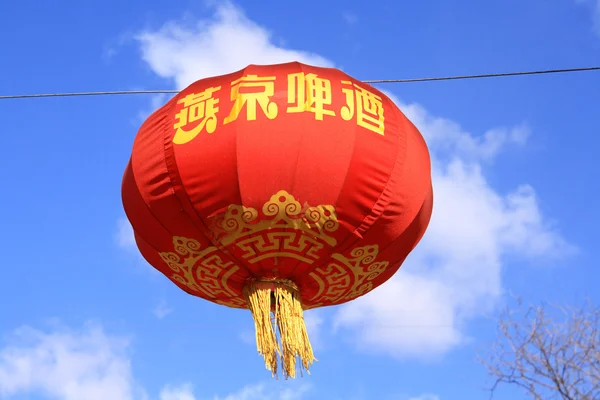 stock image A red Chinese lantern with gold characters and decorations set against a vibrant blue sky