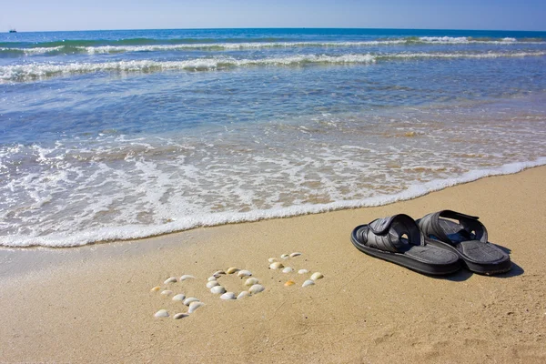 Inscription SOS in the sand with slippers — Stock Photo, Image