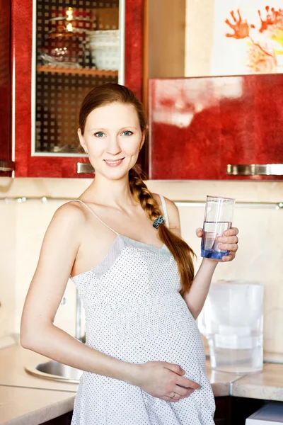 怀孕的女人在厨房里用杯水 — 图库照片