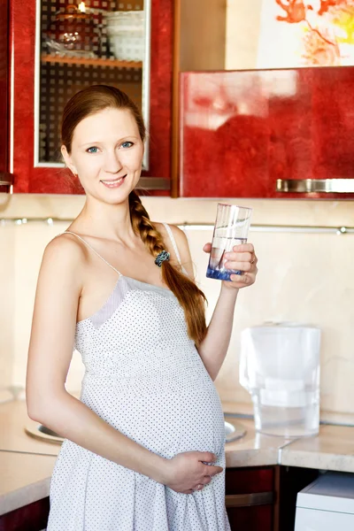 Femme enceinte dans la cuisine avec verre d'eau — Photo