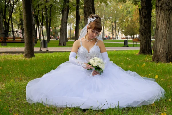 stock image Bride with bouquet sits on the grass in the park