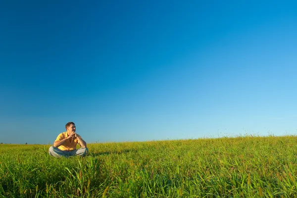 Jonge man zit op groen veld — Stockfoto