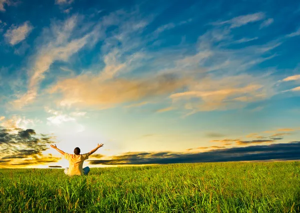Homem sentado no campo sob o pôr do sol — Fotografia de Stock