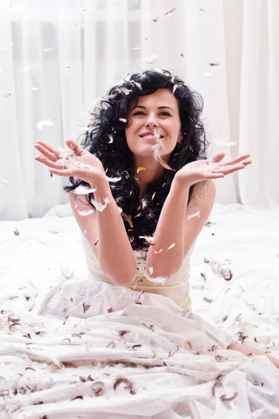 Una giovane donna sorridente catturato piume sul letto — Foto Stock