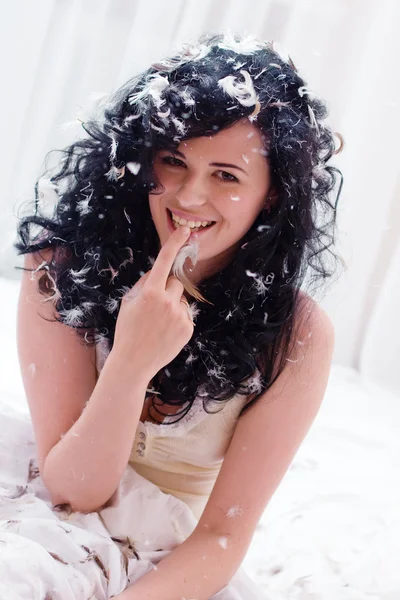 Sorridente giovane donna con piume su un letto — Foto Stock