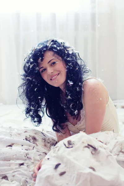 Mujer joven sonriente con plumas en una cama —  Fotos de Stock