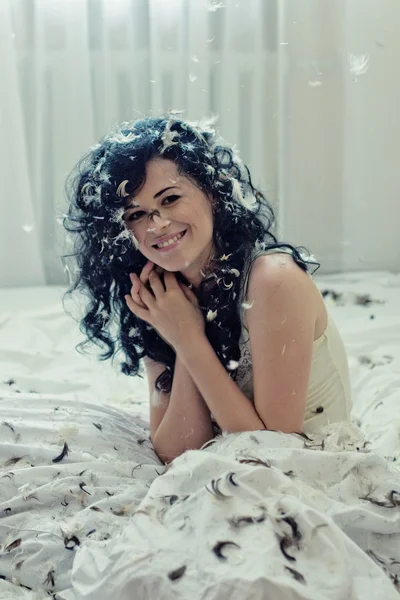 Lächelnde junge Frau mit Federn auf einem Bett — Stockfoto