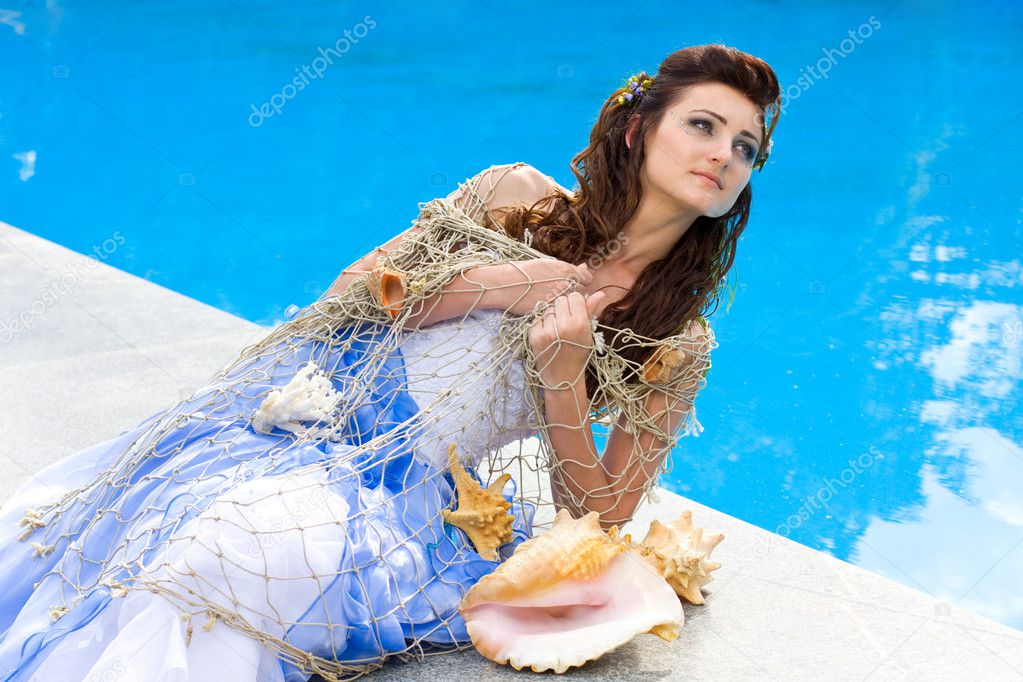 Beautiful bride posing near pool with sea shells