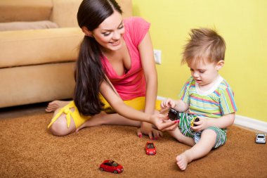 beautiful caucasian mother playing with her son with toy cars on the floor clipart