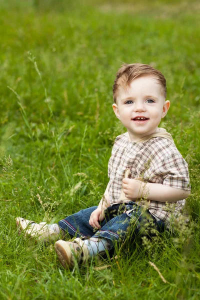 公園の緑の芝生の上に座って幸せの白人の少年 — ストック写真