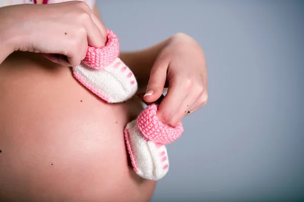 ピンクの赤ちゃんブーツのペアを保持している妊娠中の女性 — ストック写真