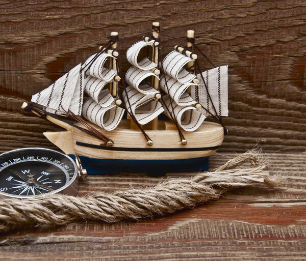 Compass, rope and model classic boat on wood background