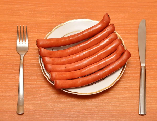 A fresh sausage on white plate with fork and knife — Stock Photo, Image