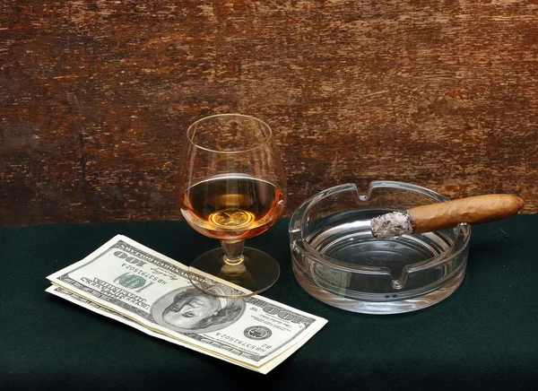 stock image Smoking cigar in an ashtray and glass cognac on green felt