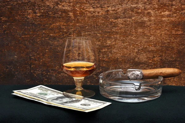 Röka cigarr i ett askfat och glas cognak — Stockfoto