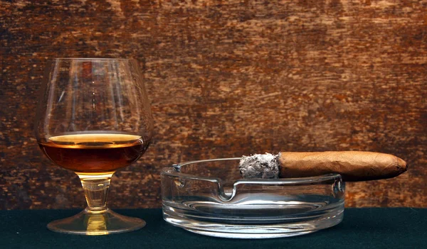 Курение сигары в пепельнице и стеклянном коньяке — стоковое фото