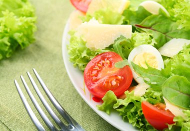 Fresh salad with tomato and quail eggs in a white bowl on a green tableclot clipart