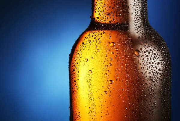 Flaska öl med droppar på en blå bakgrund. närbild av del av — Stockfoto