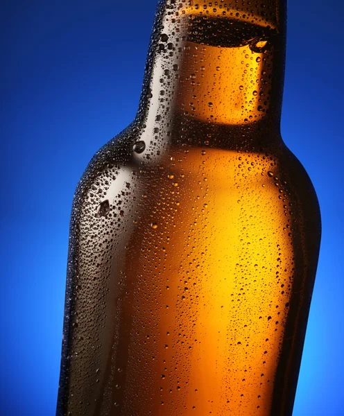 Flaska öl med droppar på en blå bakgrund. närbild av del av — Stockfoto
