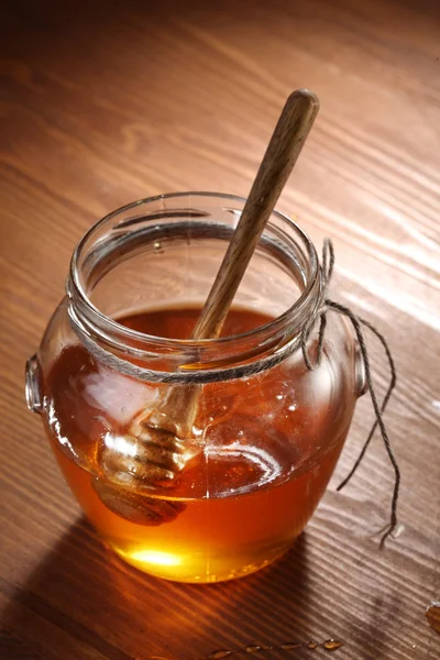 Pot met honing en houten stok in het. — Stockfoto