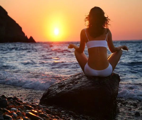 Frau meditiert am Strand bei Sonnenuntergang. — Stockfoto