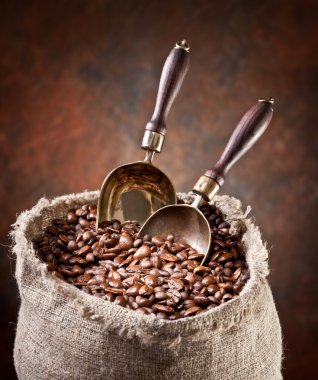 Sack of coffee beans and scoop. On a dark background. clipart