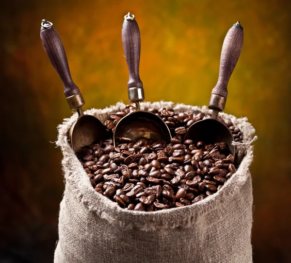 Un sac de grains de café et une cuillère. Sur un fond sombre . — Photo