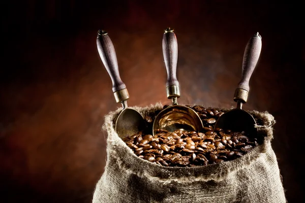 Saco de grãos de café e colher. Em um fundo escuro . — Fotografia de Stock