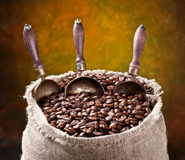 Un saco de granos de café y una cucharada. Sobre un fondo oscuro . — Foto de Stock